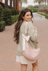 Woman with a pink bag with a bow standing on a brick path with palm trees in the background