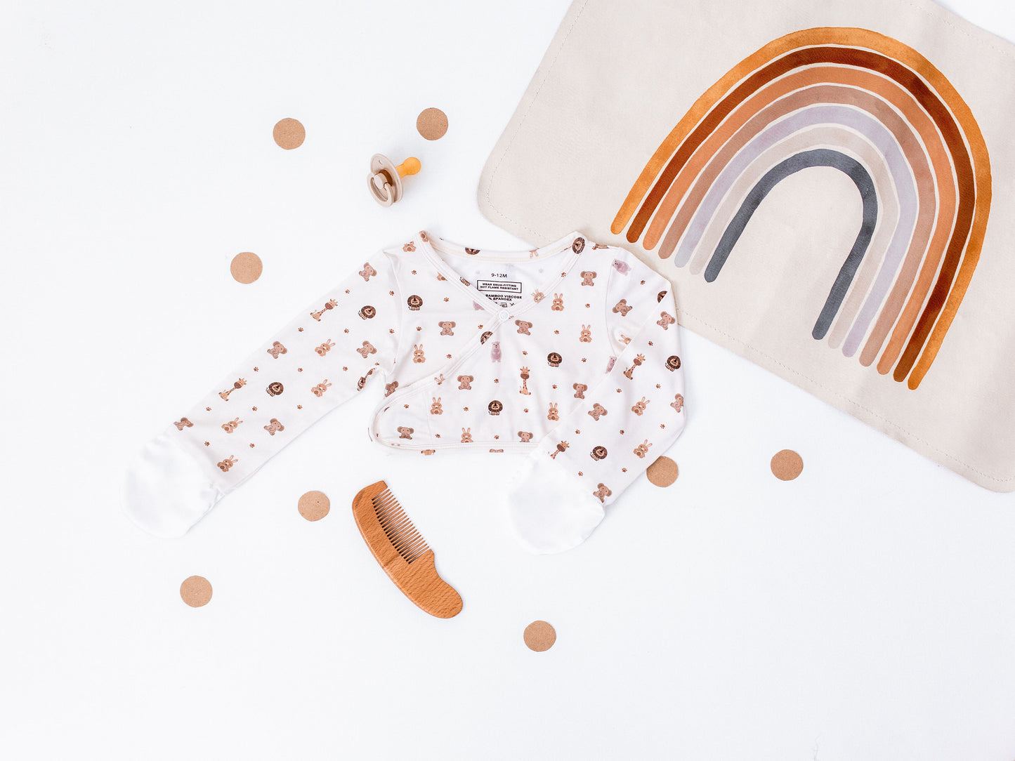 Baby outfit with long-sleeve shirt and pants, wooden comb, and rainbow-shaped pillow on a white background.